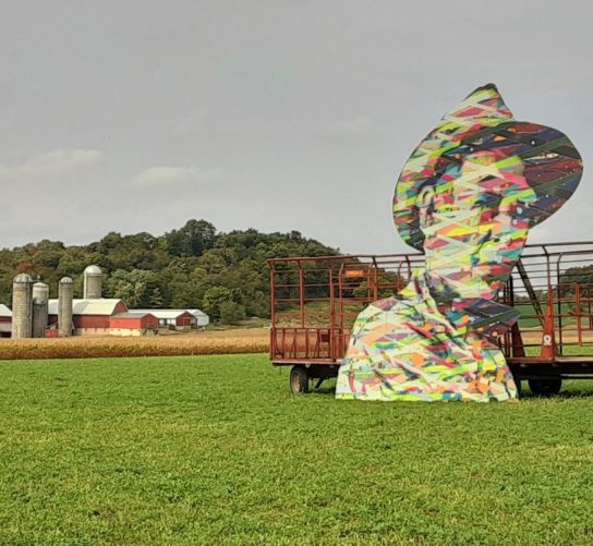 Large cut out artwork Get to the Pie by Brent Houzenga. Located in a farm field, with a farm in the background, This installation was part of the 2020 Farm Art DTour.